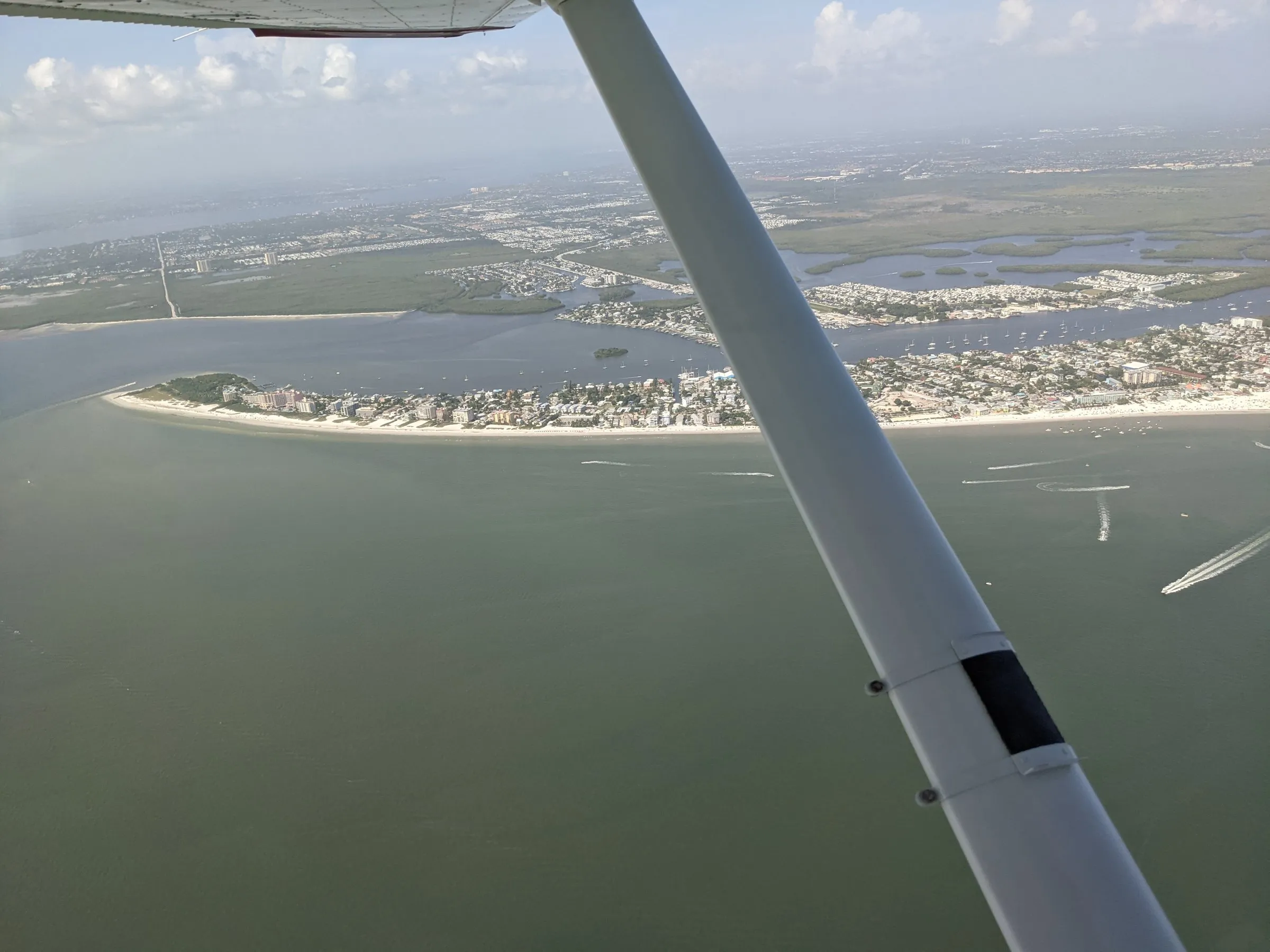Aerial view of a Southwest Florida barrier island and boats past a Cessna wing strut