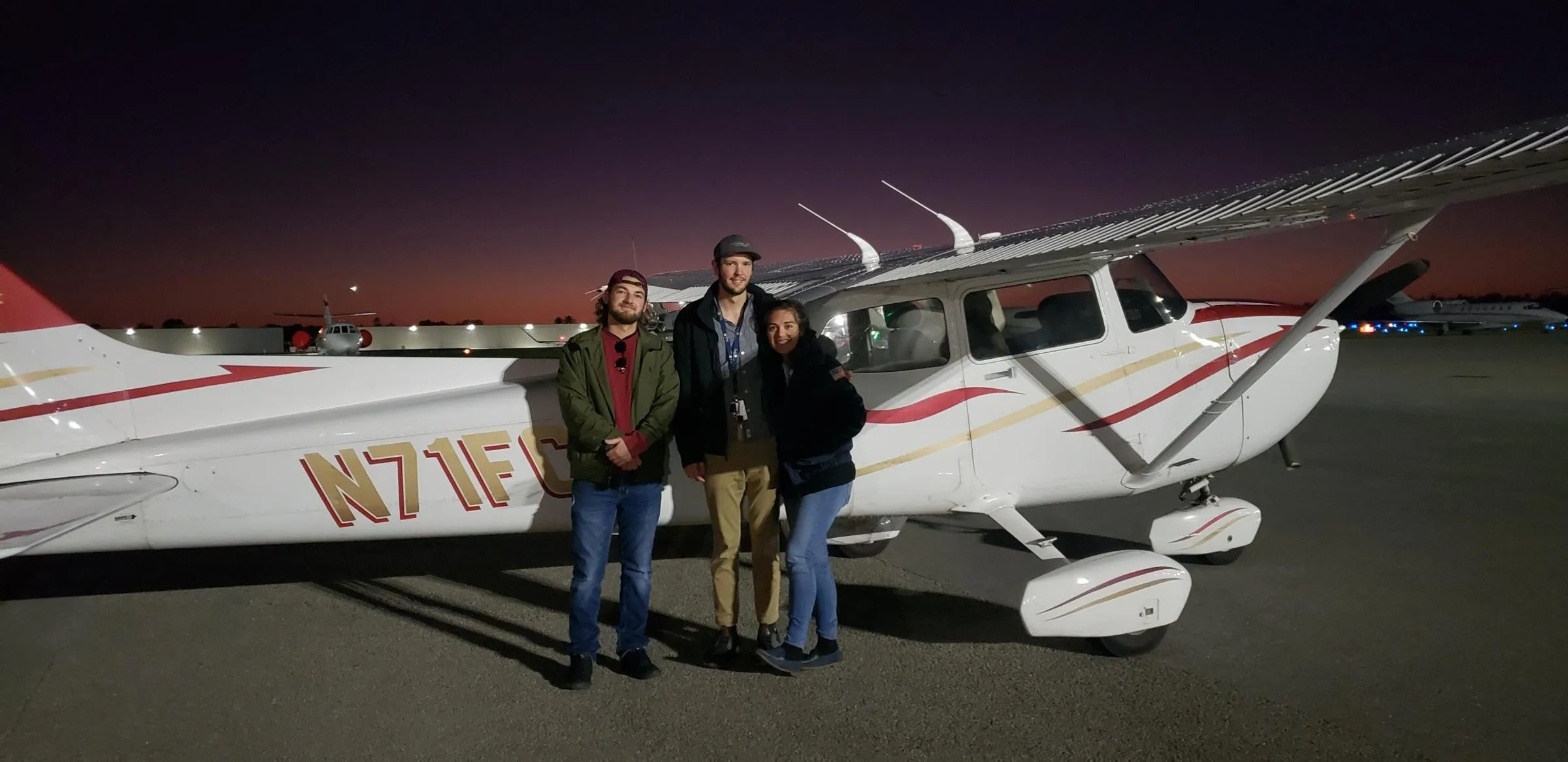 Three Naples Flying Club members beside Cessna 172R N71FC at dusk